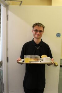 A kitchen assistant takes a lunch tray to a resident
